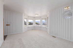 Empty room featuring wallpapered walls, a textured ceiling, carpet flooring, and visible vents