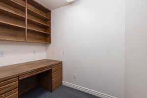 Unfurnished office featuring built in study area, baseboards, dark colored carpet, and a textured ceiling