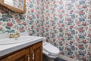 Half bath with wallpapered walls, vanity, and toilet