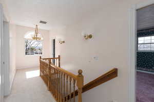 Hallway with light carpet, an upstairs landing, visible vents, and a textured ceiling