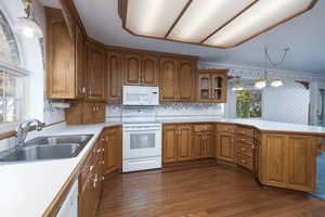 Kitchen featuring a sink, brown cabinetry, white appliances, light countertops, and dark wood-style flooring
