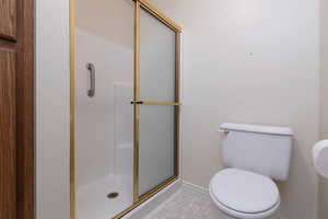 Full bathroom with a shower stall, baseboards, toilet, and tile patterned flooring