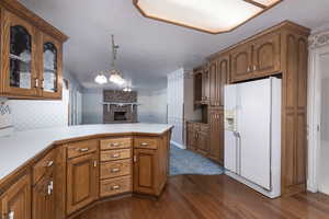 Kitchen with a peninsula, dark wood finished floors, glass insert cabinets, brown cabinetry, and white fridge with ice dispenser
