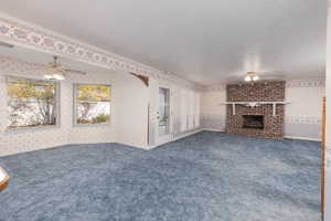 Unfurnished living room with carpet flooring, a textured ceiling, wallpapered walls, ceiling fan, and a fireplace