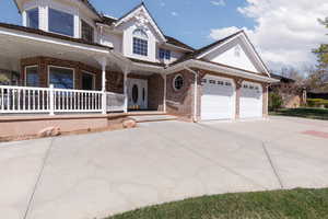 View of front of house featuring a garage, driveway, brick siding, and covered porch