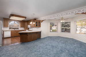Kitchen with a sink, wallpapered walls, brown cabinets, white appliances, and dark colored carpet