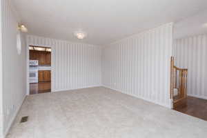 Unfurnished living room with wallpapered walls, carpet floors, visible vents, and a textured ceiling