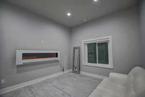 Living room featuring visible vents, baseboards, a glass covered fireplace, recessed lighting, and wood finished floors