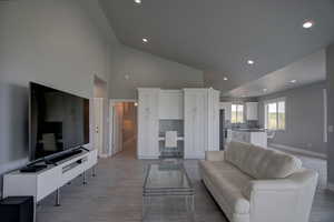 Living room with light wood-type flooring, recessed lighting, high vaulted ceiling, and baseboards