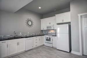 Kitchen featuring white appliances, dark countertops, a sink, white cabinetry, and visible vents