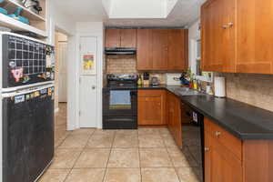 Kitchen with black appliances, brown cabinets, under cabinet range hood, and tasteful backsplash