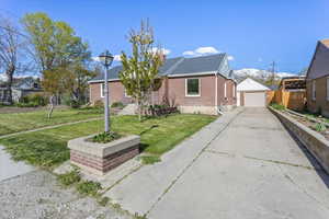 Bungalow featuring a front lawn, an outbuilding, brick siding, concrete driveway, and fence