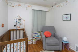 Bedroom with visible vents, a nursery area, and wood finished floors