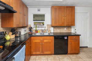 Kitchen featuring decorative backsplash, brown cabinetry, under cabinet range hood, black appliances, and a sink