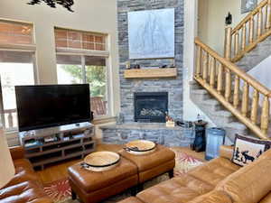 Great room area with wood finished floors, a stone fireplace, and log stairway