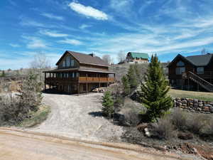 View of front of home with a wooden deck, gravel circular driveway, and stairs