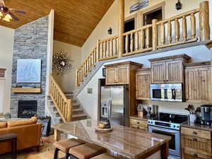 Kitchen with stainless steel appliances, a ceiling fan, a fireplace, wooden ceiling, and high vaulted ceiling