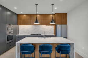 Kitchen featuring modern cabinets, a sink, tasteful backsplash, a breakfast bar area, and appliances with stainless steel finishes