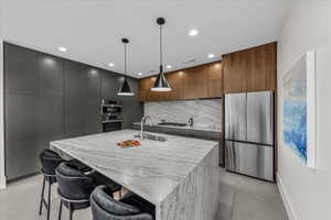 Kitchen featuring modern cabinets, a breakfast bar, stainless steel appliances, light stone countertops, and hanging light fixtures