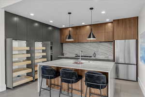 Kitchen with a breakfast bar area, modern cabinets, freestanding refrigerator, light stone countertops, and a kitchen island with sink
