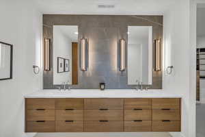 Bathroom featuring double vanity, visible vents, decorative backsplash, and a sink