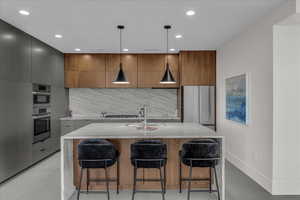 Kitchen featuring modern cabinets, light stone counters, decorative backsplash, a breakfast bar, and recessed lighting