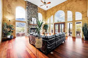 Living room with wood finished floors, ceiling fan, a fireplace, and a towering ceiling