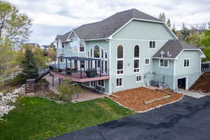 Back of property with a yard, a shingled roof, a garage, a wooden deck, and stairs
