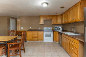 Kitchen with stainless steel appliances, brown cabinets, dark countertops, a sink, and a textured ceiling