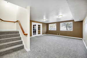 Unfurnished living room featuring french doors, baseboards, and carpet floors