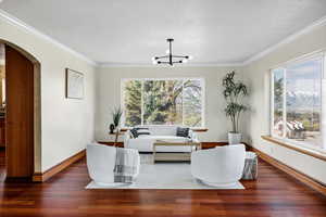 Living area with ornamental molding, a notable chandelier, wood finished floors, and arched walkways
