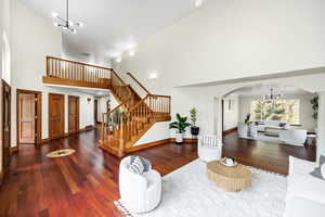 Living area featuring stairway, a chandelier, arched walkways, wood finished floors, and high vaulted ceiling