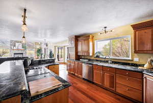 Kitchen featuring a sink, an inviting chandelier, dark wood-type flooring, a textured ceiling, and dishwasher
