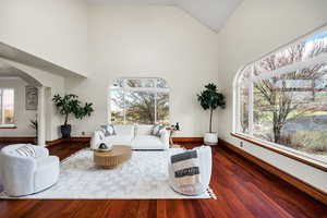 Living room with arched walkways, high vaulted ceiling, baseboards, and ornate columns