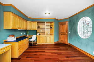 Office featuring crown molding, dark wood-style floors, built in desk, and baseboards