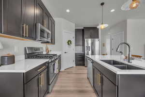 Kitchen featuring light wood finished floors, a sink, pendant lighting, light countertops, and appliances with stainless steel finishes