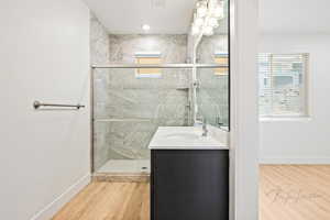 Bathroom with baseboards, wood finished floors, a shower stall, and vanity