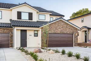 View of front of property featuring driveway, a tile roof, stone siding, an attached garage, and stucco siding