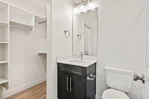 Bathroom with vanity, toilet, a walk in closet, baseboards, and wood finished floors