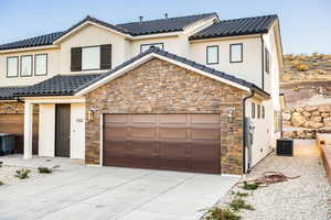 View of front of house featuring concrete driveway, stone siding, an attached garage, and a tiled roof