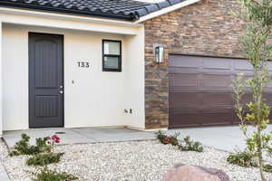 Doorway to property with a garage, stucco siding, a tile roof, and stone siding