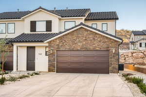 View of front of house with a tile roof, driveway, stone siding, and stucco siding