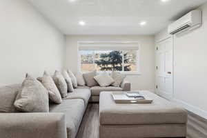 Living room with a wall mounted air conditioner, baseboards, dark wood finished floors, and recessed lighting