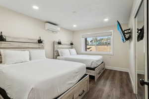 Bedroom featuring dark wood-type flooring, a wall mounted air conditioner, recessed lighting, and baseboards