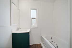 Full bath with wood finished floors, a tub to relax in, and vanity