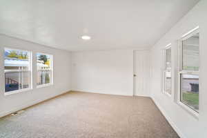 Empty room with light colored carpet, visible vents, and baseboards