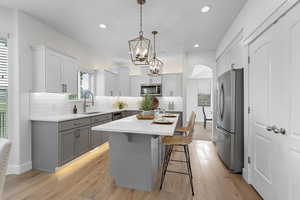 Kitchen featuring gray cabinets, appliances with stainless steel finishes, light countertops, a sink, and a center island