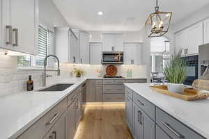Kitchen featuring gray cabinets, light stone counters, appliances with stainless steel finishes, light wood finished floors, and a sink