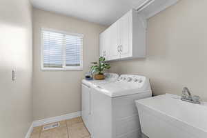Washroom with washing machine and dryer, a sink, visible vents, baseboards, and cabinet space