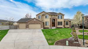 Traditional-style home featuring a front lawn, an attached garage, driveway, stucco siding, and fence